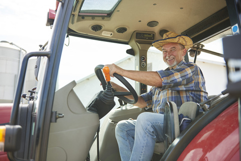 Porträt eines lächelnden älteren Landwirts auf einem Traktor, lizenzfreies Stockfoto