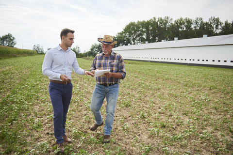 Landwirt und Geschäftsmann besprechen die Daten des Klemmbretts auf dem Feld, lizenzfreies Stockfoto
