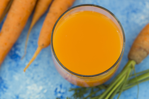 Glas mit frischem Karottensaft und Karotten auf hellblauem Grund, lizenzfreies Stockfoto