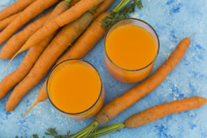 Zwei Gläser mit frischem Karottensaft und Karotten auf hellblauem Grund - JUNF01237