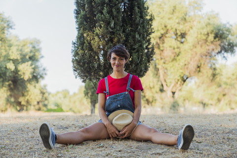 Porträt einer lächelnden Frau, die in der Natur auf dem Boden sitzt, lizenzfreies Stockfoto