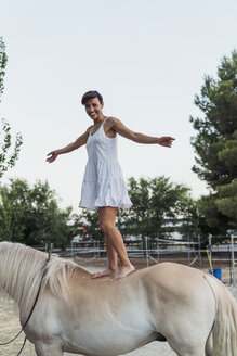 Porträt einer lächelnden Frau, die barfuß auf einem Pferd balanciert - KKAF01614