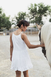 Rückenansicht einer Frau im weißen Kleid, die ein Pferd führt - KKAF01617