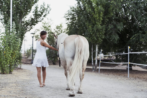 Lächelnde Frau in weißem Kleid führt Pferd - KKAF01618