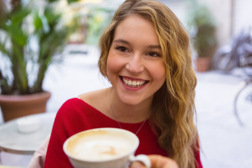 Porträt einer lachenden jungen Frau mit Teetasse in einem Straßencafé - MGIF00236