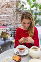 Young woman sitting at pavement cafe using smartphone - MGIF00239