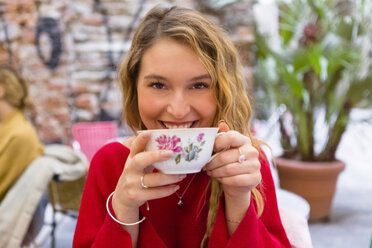Porträt einer lächelnden jungen Frau, die in einem Straßencafé eine Tasse Tee trinkt - MGIF00240