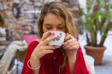 Porträt einer jungen Frau, die in einem Straßencafé eine Tasse Tee trinkt - MGIF00241