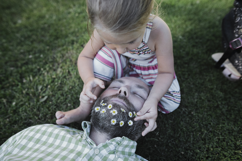 Little girl decorating father's beard with daisies on meadow in the garden stock photo