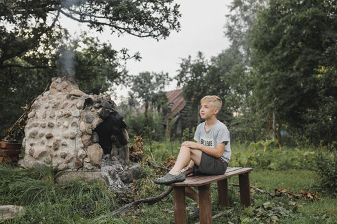 Junge entspannt sich auf einer Holzbank im Garten - KMKF00476