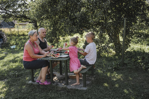 Großeltern verbringen Zeit mit Enkel und Enkelin im Garten und essen Wassermelone - KMKF00482