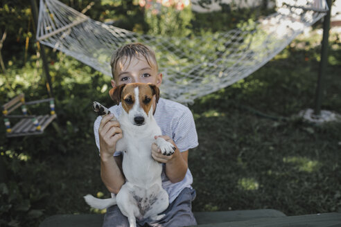 Junge sitzt mit Jack Russel Terrier auf dem Schoß im Garten - KMKF00483