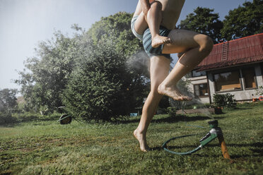 Brother and sister playing with garden hose in garden - KMKF00493