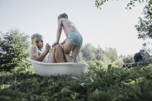 Bruder und Schwester spielen mit Wasser in einer kleinen Badewanne im Garten - KMKF00495