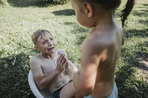 Bruder und Schwester spielen mit Wasser in einer kleinen Badewanne im Garten - KMKF00496