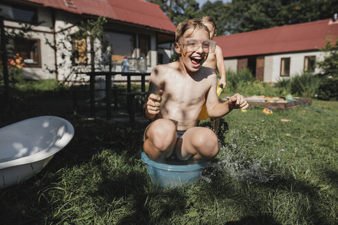 Glückliche Geschwister spielen mit Wasser im Garten - KMKF00503