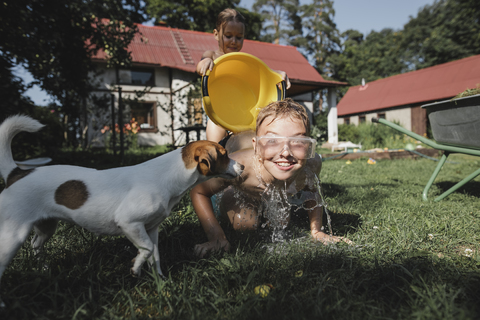 Bruder, Schwester und Hund spielen mit Wasser im Garten, lizenzfreies Stockfoto