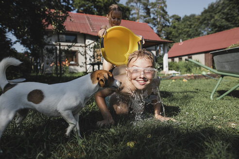 Bruder, Schwester und Hund spielen mit Wasser im Garten - KMKF00506