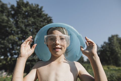 Nasser Junge mit Schutzbrille, der im Garten eine Schüssel über seinem Kopf hält, lizenzfreies Stockfoto