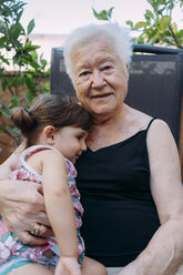 Porträt einer lächelnden Großmutter, die mit ihrer kleinen Tochter auf der Terrasse sitzt - GEMF02371