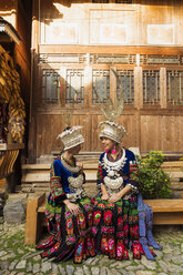 China, Guizhou, zwei lächelnde junge Miao-Frauen in traditionellen Kleidern und Kopfbedeckungen - KKAF01627