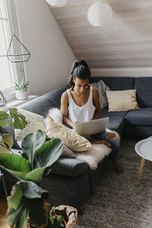 Smiling young woman sitting on the couch at home using laptop - LHPF00005