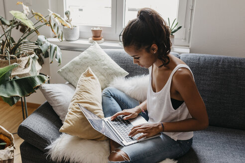 Junge Frau sitzt zu Hause auf der Couch und benutzt einen Laptop - LHPF00007