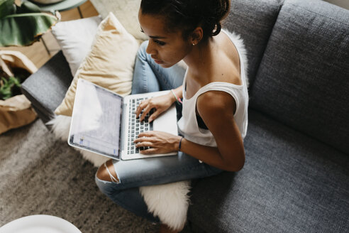 Junge Frau sitzt zu Hause auf der Couch und benutzt einen Laptop - LHPF00008