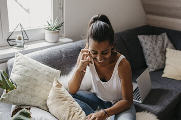 Lächelnde junge Frau am Telefon, die zu Hause auf der Couch sitzt - LHPF00012