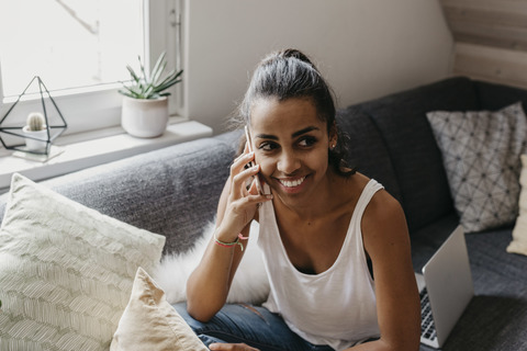 Portrait of smiling young woman on the phone sitting on the couch at home stock photo