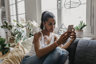 Porträt einer jungen Frau, die zu Hause auf der Couch sitzt und ein Selfie mit ihrem Mobiltelefon macht - LHPF00016