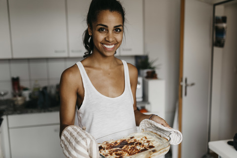 Porträt einer lächelnden jungen Frau mit einer Kasserolle in der Küche, lizenzfreies Stockfoto