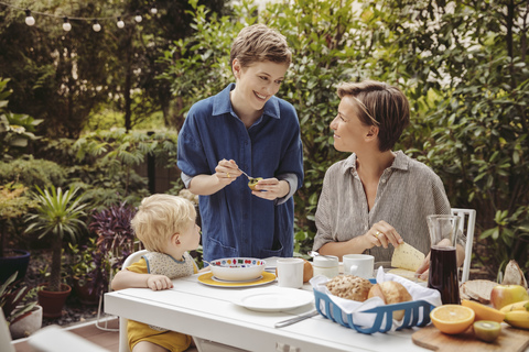 Zwei glückliche Mütter am Frühstückstisch im Freien mit ihrem Kind, lizenzfreies Stockfoto