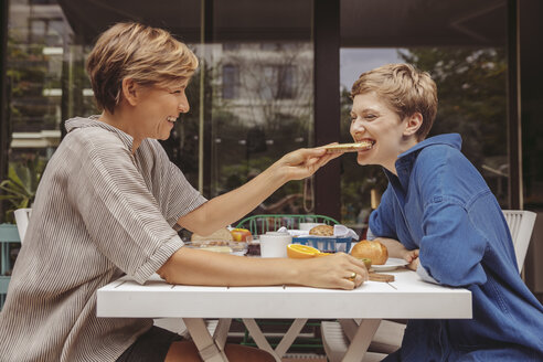 Zwei glückliche Frauen am Frühstückstisch auf ihrer Terrasse - MFF04420