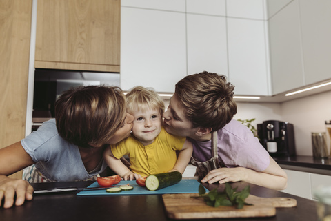 Happy lesbian couple kissing their child in kitchen stock photo