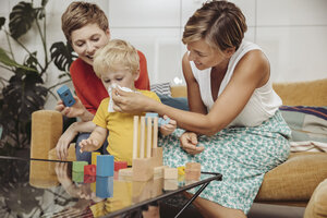 Two mothers playing with their child at home, cleaning nose with tissue - MFF04430