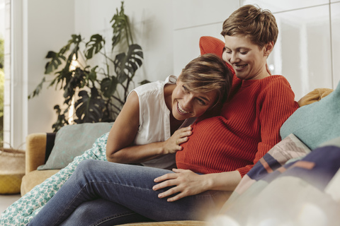 Happy lesbian couple feeling movements of baby belly of the expectant mother stock photo