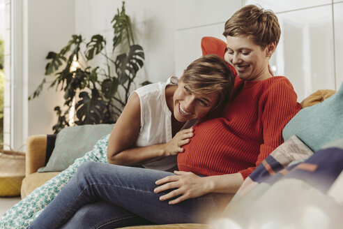 Glückliches lesbisches Paar fühlt die Bewegungen des Babybauchs der werdenden Mutter - MFF04443