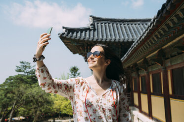 South Korea, Gyeongju, happy woman taking a selfie with cell phone in Bulguksa Temple - GEMF02397