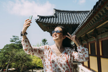 South Korea, Gyeongju, happy woman taking a selfie with cell phone in Bulguksa Temple - GEMF02398