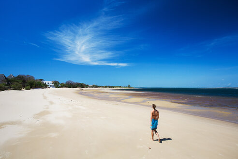 MANDA ISLAND, LAMU, INDIAN OCEAN, KENIA, AFRIKA: Eine junge Frau geht an einem leeren weißen Strand unter strahlend blauem Himmel entlang. - AURF03360