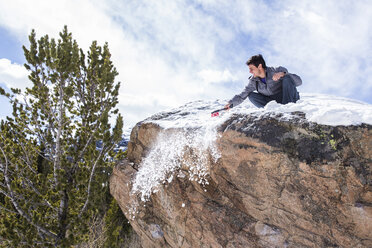 Männlicher Bergsteiger reinigt die Spitze eines Felsblocks von Schnee im Rocky Mountain National Park, Colorado - AURF03371
