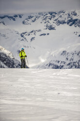 Skifahrer steht am Rande eines steilen Abhangs im Devero-Tal mit schneebedeckten Bergen im Hintergrund an einem bewölkten Tag. Baceno, Piemonte, Ossola. - AURF03539