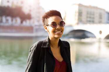 Italien, Verona, Porträt einer lächelnden jungen Frau vor dem Fluss Etsch - GIOF04266