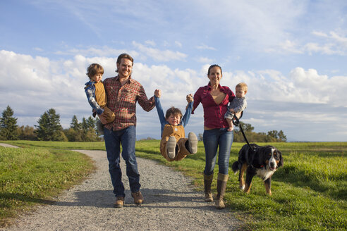 Eine fünfköpfige Familie mit Hund geht spielerisch einen Kiesweg in einem örtlichen Park entlang. - AURF03613