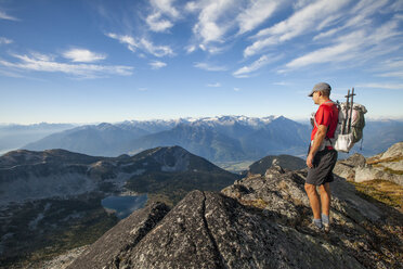 A backpacker looks down at Valentine Lake from a rocky ridge near Saxifrage Mountain, Pemberton, British Columbia, Canada. - AURF03621