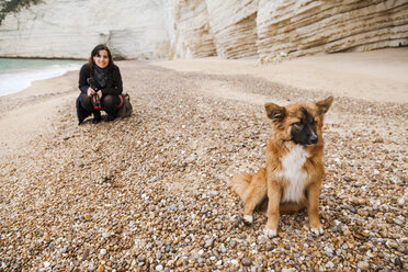 Italien, Vieste, streunender Hund am Strand von Vignanotica, während eine lächelnde Frau im Hintergrund hockt - FLMF00008