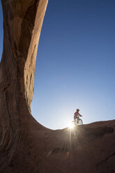 A girl riding a mountain bike along Wilson Arch near Moab, Utah. - AURF03659