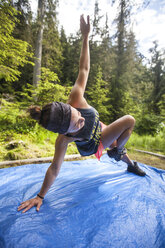 Eine fitte Frau absolviert ihr morgendliches Trainingsprogramm auf einer blauen Plane beim Camping im Bowron Lake Provincial Park. - AURF03685