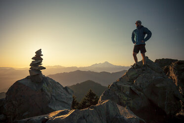 A hiker stands on a large rock, opposite the summit cairn or Sauk Mountain. - AURF03690